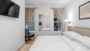Une chambre avec un grand lit, un téléviseur fixé au mur, un miroir et une fenêtre avec des rideaux.