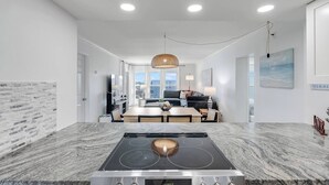 Una cocina moderna con una isla central, un comedor y una sala de estar con sofá y televisor.