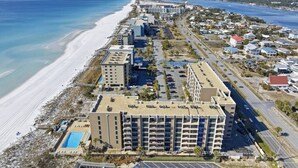 Vista aérea de un hotel frente al mar con varias construcciones, una playa y un estacionamiento.