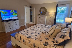 Un dormitorio con cama, televisión, cómoda, espejo y ventana con cortinas.