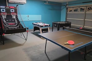 Ein Raum mit einem Tischtennisch, einem Kicker und einem Basketballkorb.