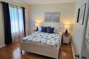 A bedroom with a bed, two bedside tables, a door, and a window with curtains. - Private Pool • 5 Min to Beach • Game Room • BBQ (Panama City Beach)
