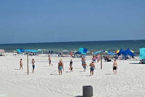 Una playa con gente jugando voleibol, sombrillas y sillas de playa.