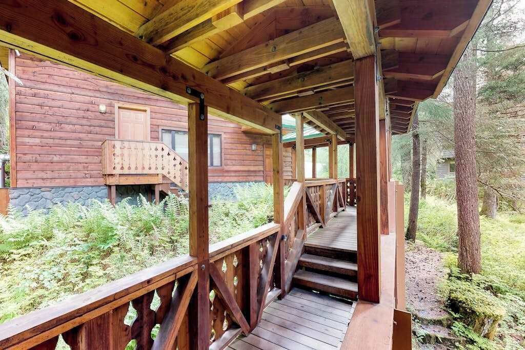 Een houten terras dat leidt naar een chalet met een stenen fundering, omgeven door groen.