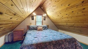 A bedroom with a sloped ceiling, a bed with a floral bedspread, a nightstand, a dresser, and a window with blinds.