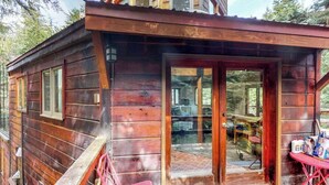 Eine Holzhütte mit Glastür, einer kleinen Veranda und einem Tisch mit Gegenständen darauf.
