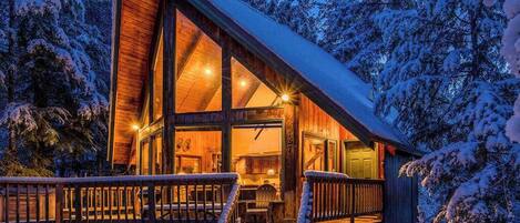 Une cabane en bois dotée de grandes fenêtres, d’une terrasse et d’un escalier menant à l’entrée.