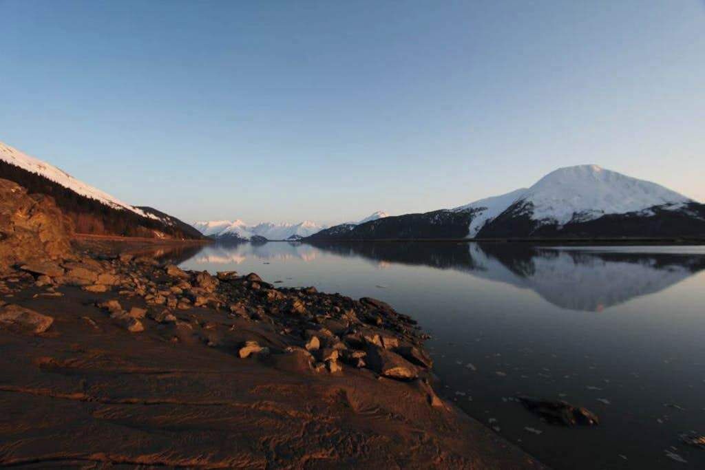 A calm lake with a snow-capped mountain in the background and rocky terrain in the foreground.