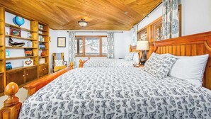 Una camera da letto con soffitto in legno, un letto grande con biancheria a motivi, una libreria in legno e una finestra con tende.