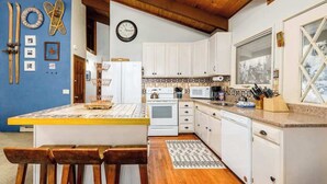 Una cucina con mobili bianchi, soffitto in legno e una grande finestra.
