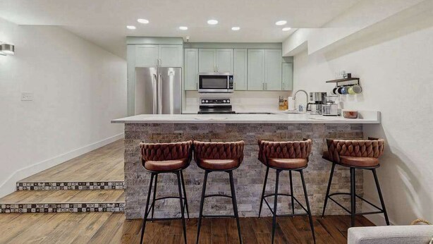 A modern kitchen with a central island, bar stools, and a microwave. - First Tracks Chalet | Renovated Base Condo (Girdwood)