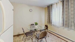 Uma sala de jantar com uma mesa redonda de vidro, quatro cadeiras, um relógio na parede e cortinas estampadas.