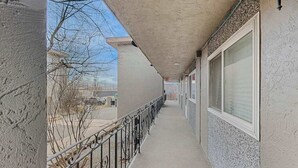 Um corredor com piso de concreto, corrimão de metal e fachada de prédio com janelas e parede texturizada.