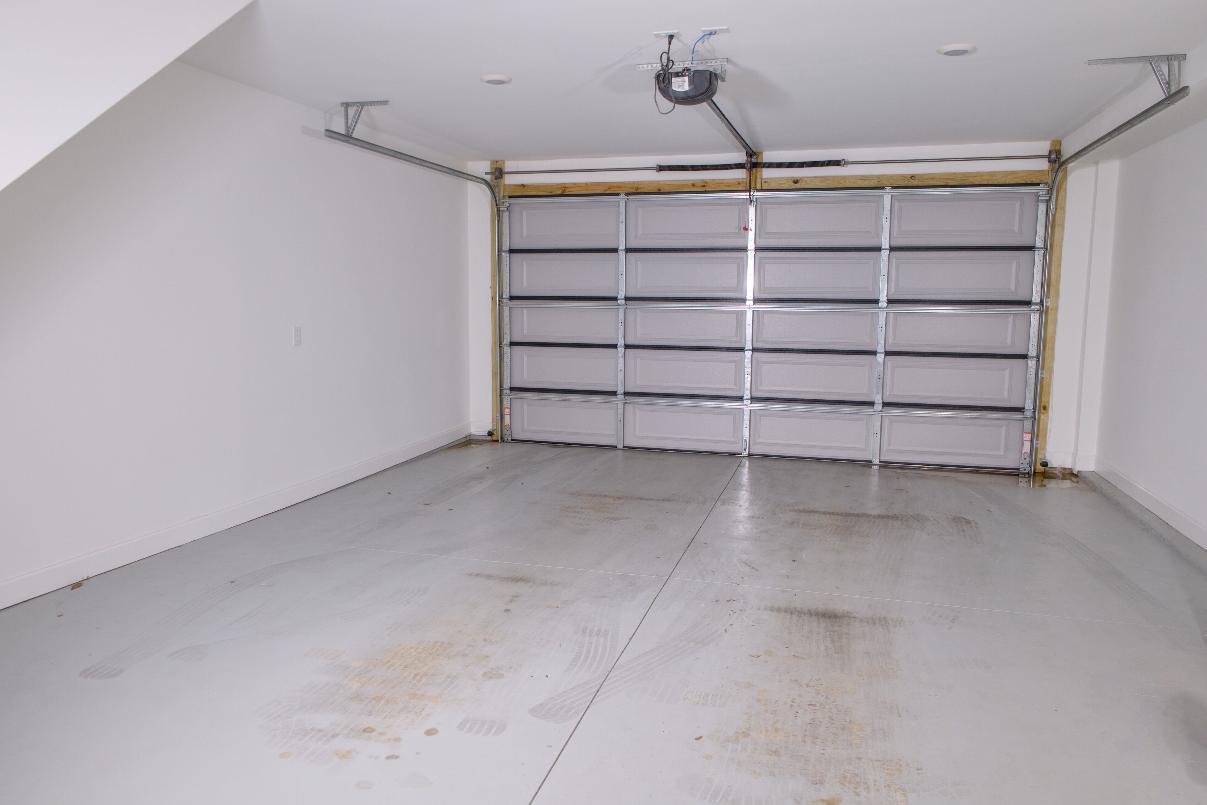 A garage with a closed garage door, a ceiling light, and a visible electrical outlet.