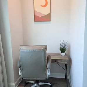 Ein Büro mit Eckausrichtung, ein grauer Bürostuhl, ein Holztisch und ein Wandbild.