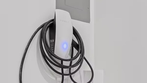 Una estación de carga Tesla con una pared blanca y un tablero eléctrico gris.