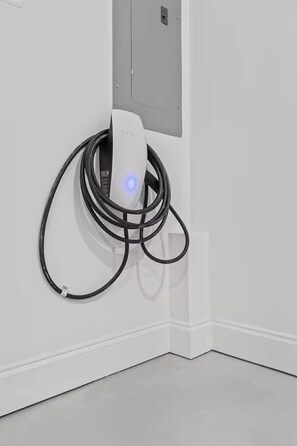 Una estación de carga Tesla con una pared blanca y un tablero eléctrico gris.