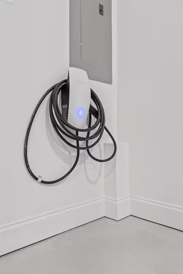 Eine Tesla Ladestation mit weißer Wand und einem grauen Stromverteiler.