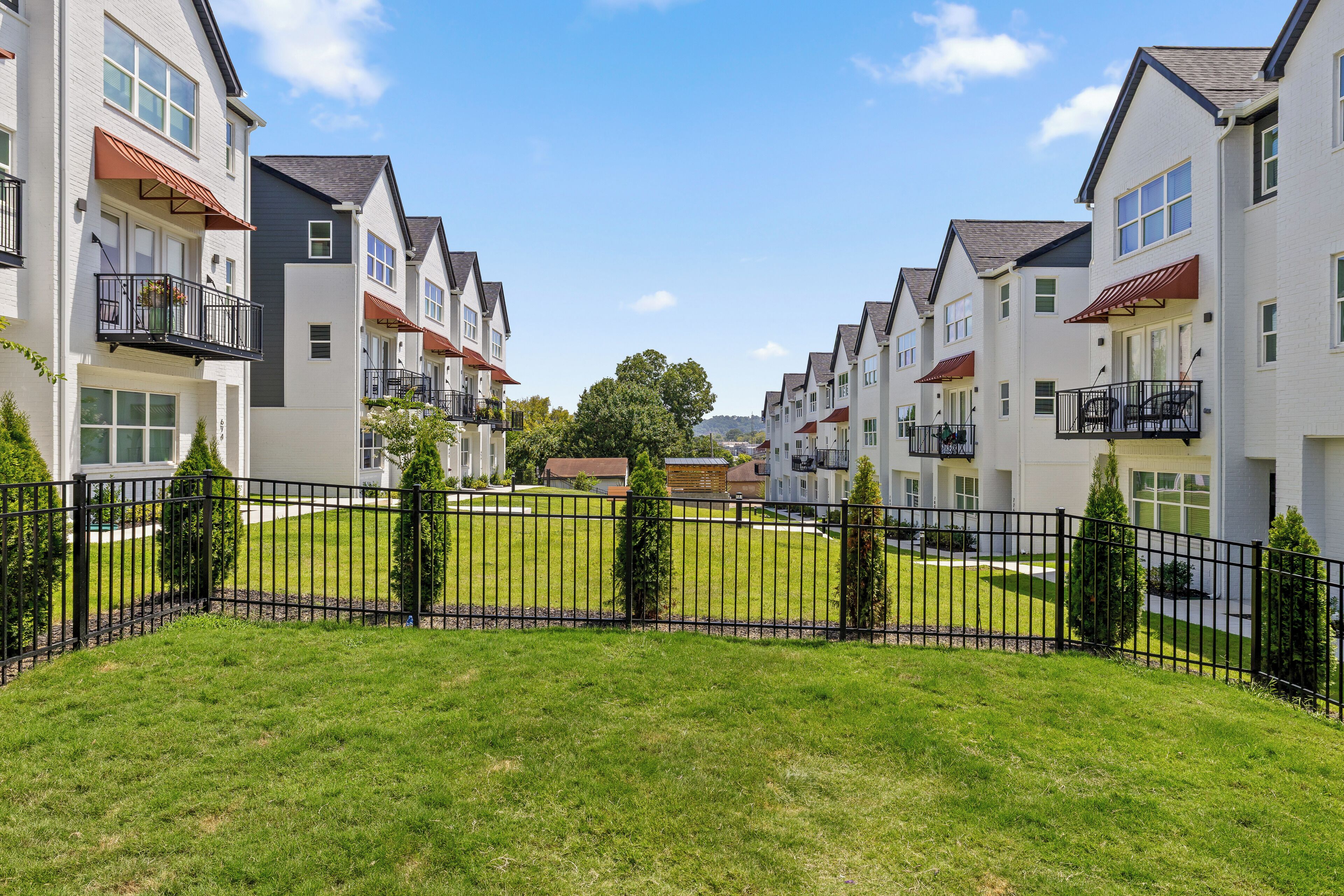 A row of modern apartment buildings with balconies, a well-maintained lawn, and a clear sky.