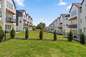 A row of modern apartment buildings with balconies, a well-maintained lawn, and a clear sky.