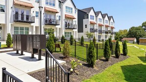 Un hilera de edificios de apartamentos modernos con balcones, un patio cercado y buzones.
