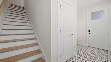A staircase with wooden steps leading to a landing, a white door with a window, and a tiled floor with a geometric pattern.