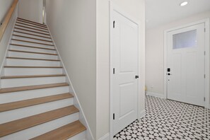 A staircase with wooden steps leading to a landing, a white door with a window, and a tiled floor with a geometric pattern.