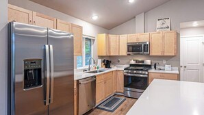 A modern kitchen with stainless steel appliances, wooden cabinets, and a white countertop. - Penguin Ridge Estate | Full 4BR Duplex Compound (Girdwood)