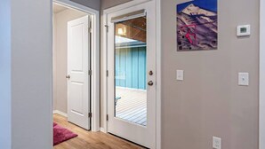 A hallway with a white door, a glass door leading to a balcony, and a poster on the wall. - Penguin Ridge Estate | Full 4BR Duplex Compound (Girdwood)
