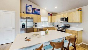 Une cuisine moderne dotée d’un îlot central, d’appareils électroménagers en acier inoxydable, de meubles en bois et d’un plan de travail blanc.