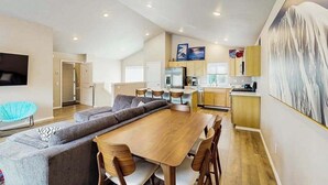 Un salon moderne avec une table à manger en bois et des canapés gris, une cuisine avec des meubles en bois et une grande peinture abstraite accrochée au mur.