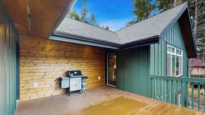 Une cabane en bois dotée d’une terrasse, d’un barbecue et d’une porte donnant accès à un espace intérieur.