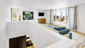 Een moderne woonkamer met een bank, een flatscreen televisie, een houten kast en een groot raam met gordijnen.