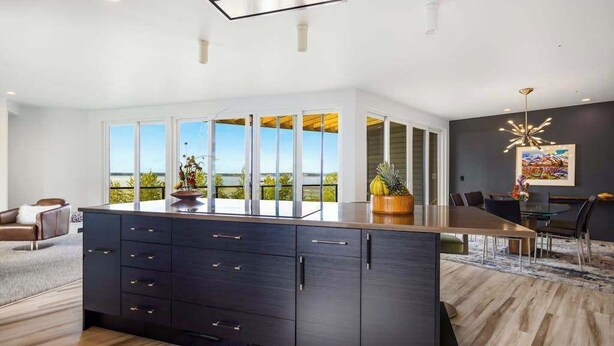 Een moderne keuken met een groot eiland, een eethoek met tafel en stoelen, en uitzicht op de omgeving.