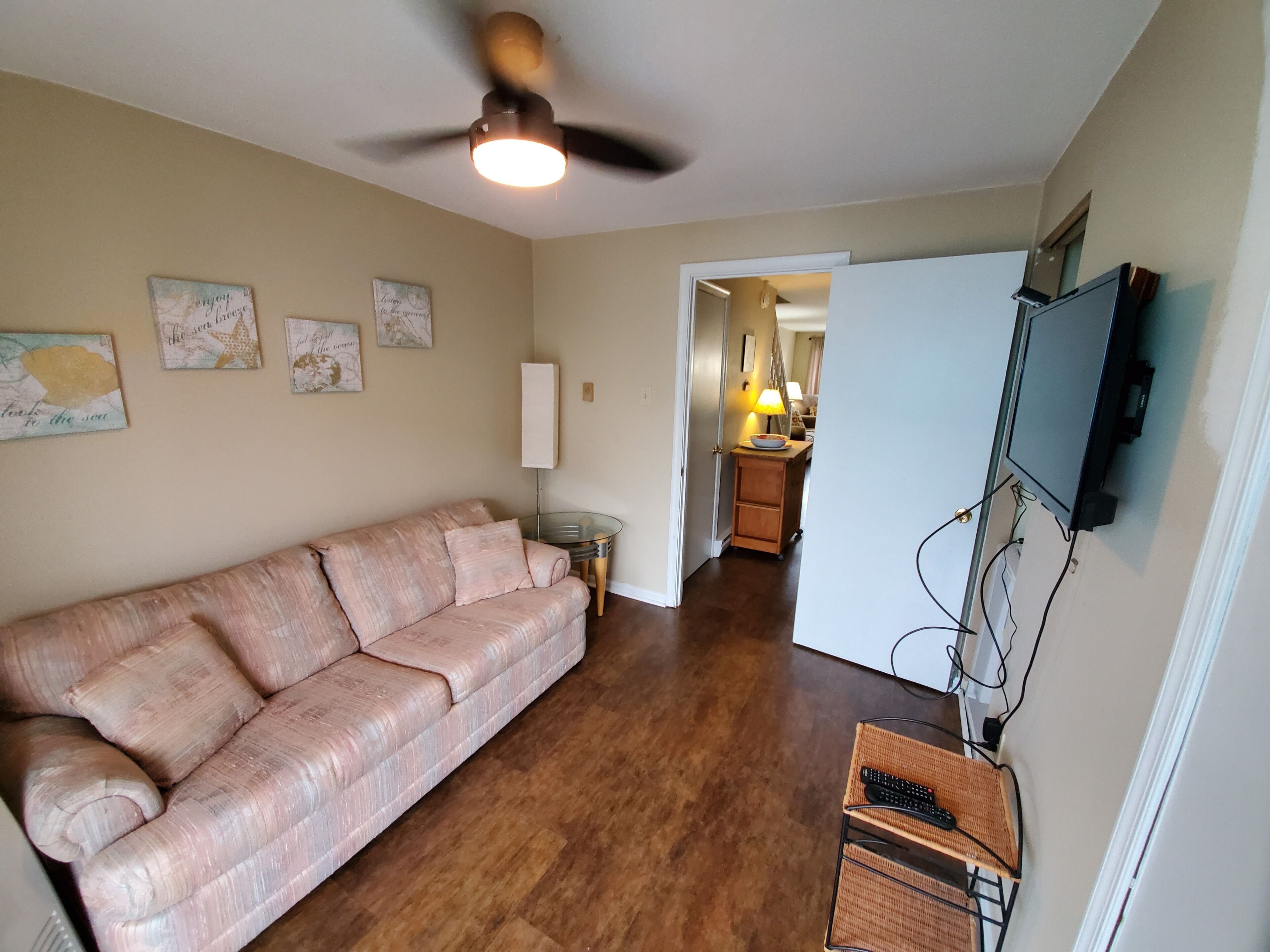 Un salon avec un canapé, un ventilateur de plafond, un téléviseur et, au fond, un coin repas.