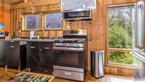 A kitchen with wooden walls, a stainless steel stove, a microwave, and a refrigerator. - Alpine Meadows A-Frame | Walk to Slopes (Girdwood)