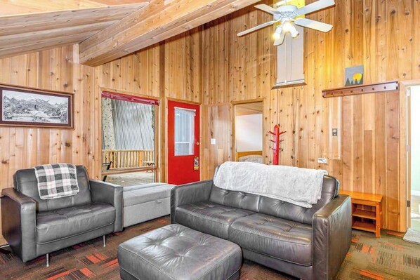 A wooden-paneled room with a sofa, a small table, and a ceiling fan.