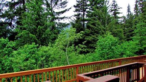 A wooden deck with a view of dense green forest. - North 413 | True Ski-In/Out | Gas Fireplace (Girdwood)