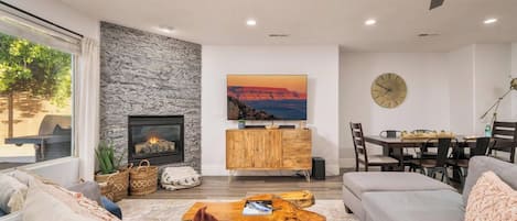A modern living room with a fireplace, a dining area, and a large window.