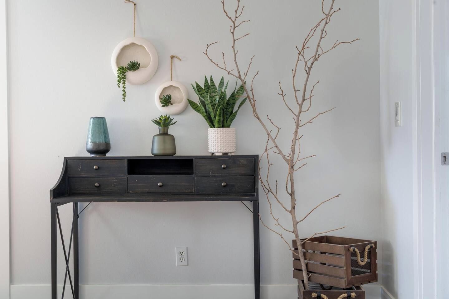 A room with a dark wooden desk, a potted plant, and wall-mounted shelves with decorative items.