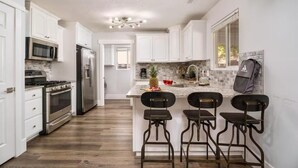 A modern kitchen with white cabinets, stainless steel appliances, a wooden floor, and a bar area with stools. - Family Getaway: 4BR, Pool & Spa, – Sleeps 10 (La Verkin)
