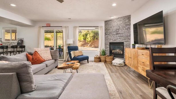 A modern living room with a sofa, armchair, TV, fireplace, and dining area. - Family Getaway: 4BR, Pool & Spa, – Sleeps 10 (La Verkin)