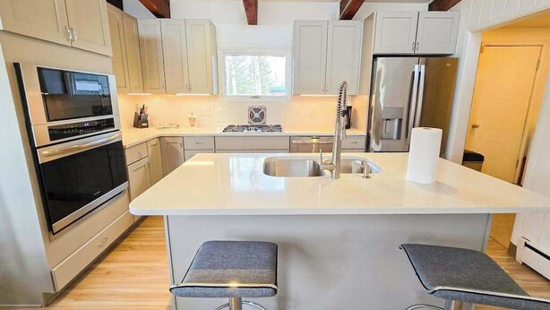 Een moderne keuken met witte kastjes, een centraal eiland met een spoelbak, een fornuis en een koelkast. Er staan twee barkrukken bij het eiland.