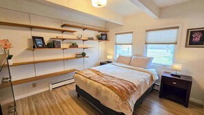 Een slaapkamer met een bed, houten vloer, inbouwkasten, nachtkastjes en een raam.