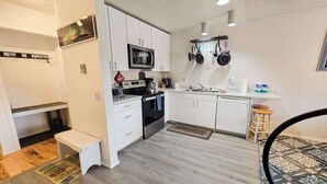 Una cocina pequeña con armarios blancos, microondas, estufa y utensilios colgados.