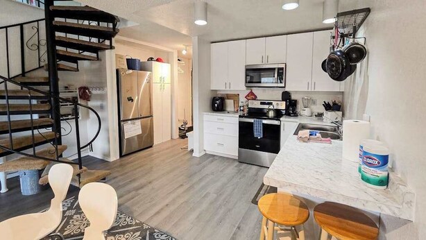 Una cocina compacta con microondas integrado, un refrigerador de acero inoxidable y una barra con taburetes.