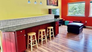 Une cuisine aux couleurs rouge et jaune, avec un mur de fond en briques, des tabourets en bois et une grande fenêtre.