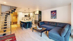 Een moderne woonkamer met een bank, een salontafel en een keukenhoek met een eettafel en stoelen.
