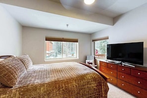 A bedroom with a bed, a TV on a wooden dresser, and a window with a view of trees. - Hanging Glacier Chalet - Group Lodge - Sauna (Girdwood)