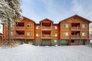 A multi-story wooden lodge with balconies, a stone foundation, and a snow-covered ground. - Hanging Glacier Chalet - Group Lodge - Sauna (Girdwood)